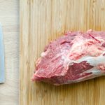 Steak on a cutting board with a knif on the left.