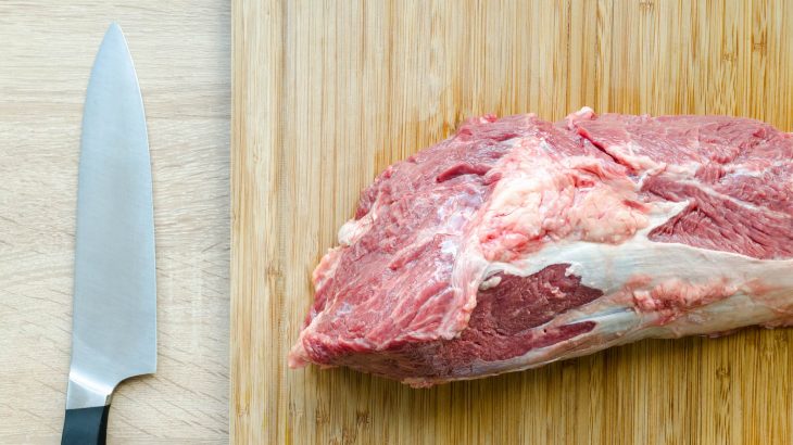 Steak on a cutting board with a knif on the left.