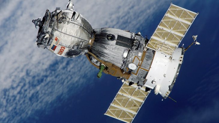 A Russian soyuz satellite orbiting over earth, see with clouds in the background.