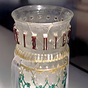 Glass openwork vessel from 300–350 CE with inscription and symbol. Inscription: ΠΙΕ ΖΗCΑΙC ΚΑΛWC ΑΕΙ (Drink, may you live well always!) Credit: of Hallie G. Meredith/WSU
